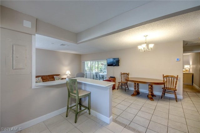 kitchen with light tile patterned flooring, a kitchen bar, a chandelier, a textured ceiling, and kitchen peninsula