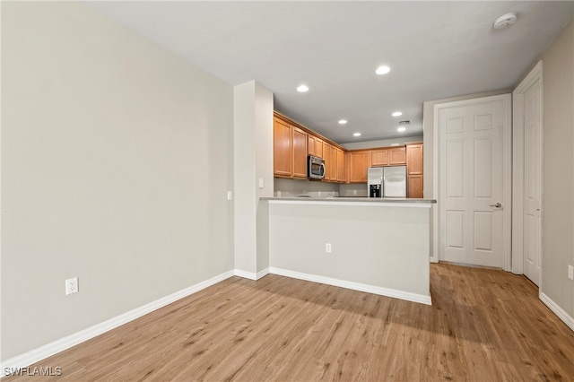 kitchen with light wood-type flooring, stainless steel appliances, and kitchen peninsula