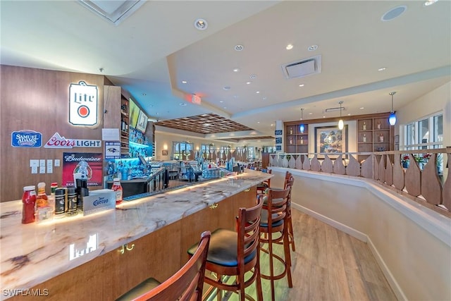 bar featuring light wood-type flooring, light stone counters, and decorative light fixtures