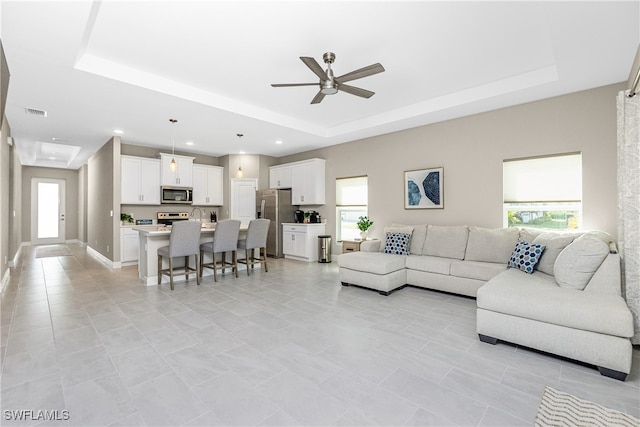 tiled living room featuring ceiling fan, a tray ceiling, and a wealth of natural light