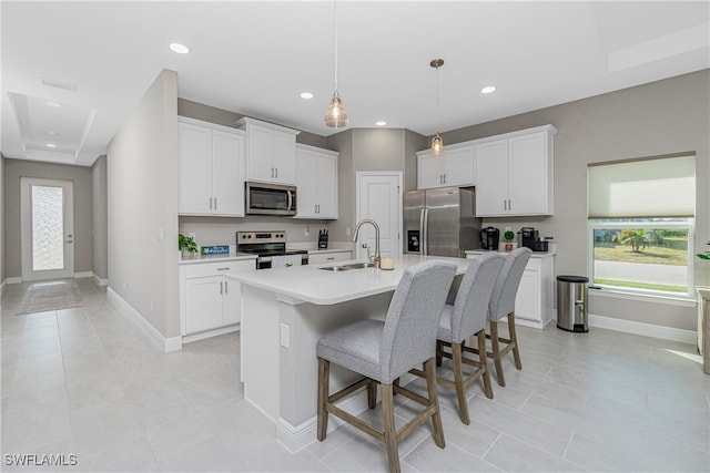 kitchen with appliances with stainless steel finishes, sink, decorative light fixtures, white cabinets, and a kitchen island with sink