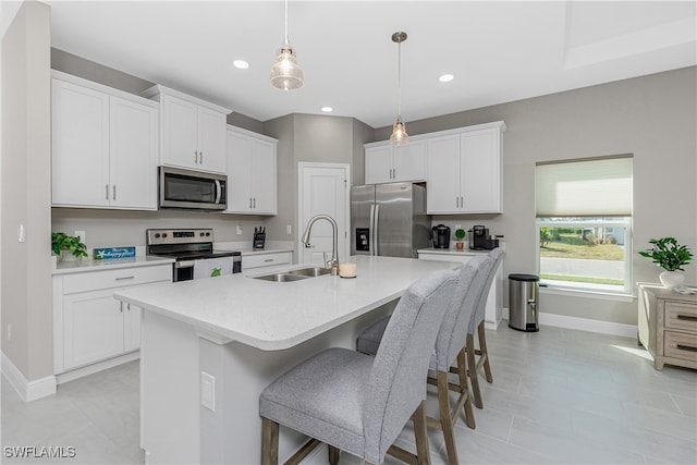 kitchen featuring a center island with sink, sink, decorative light fixtures, white cabinetry, and appliances with stainless steel finishes