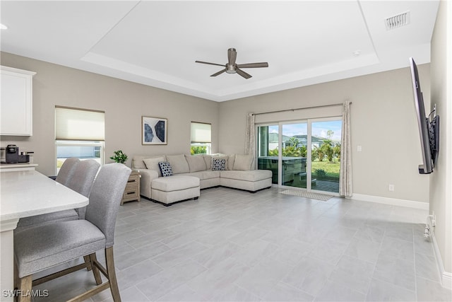 living room featuring light tile patterned flooring, ceiling fan, and a raised ceiling