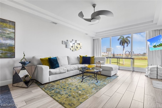 living room featuring light hardwood / wood-style flooring, a tray ceiling, and ceiling fan