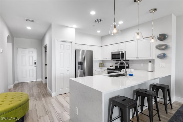 kitchen featuring kitchen peninsula, stainless steel appliances, sink, decorative light fixtures, and white cabinetry