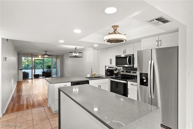 kitchen with kitchen peninsula, stainless steel appliances, sink, pendant lighting, and white cabinets