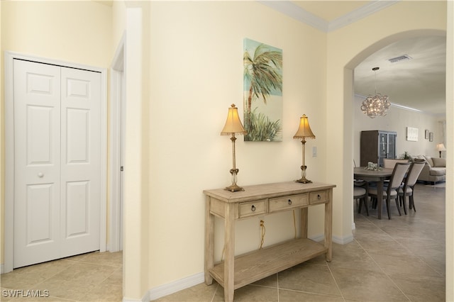 corridor with ornamental molding, an inviting chandelier, and light tile patterned floors