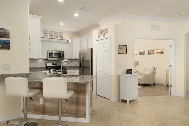 kitchen with a kitchen breakfast bar, kitchen peninsula, stainless steel appliances, light stone countertops, and white cabinetry