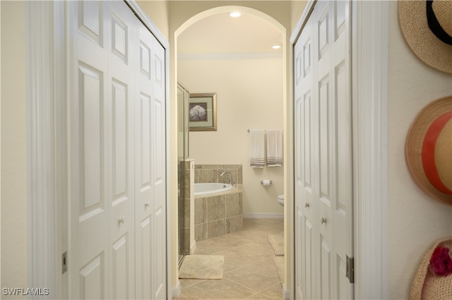 bathroom with crown molding, toilet, tiled bath, and tile patterned flooring