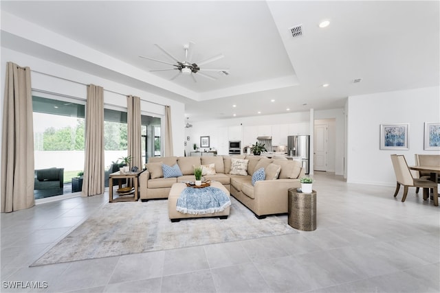 tiled living room featuring ceiling fan and a tray ceiling