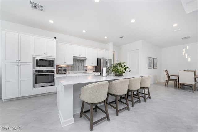 kitchen featuring white cabinetry, appliances with stainless steel finishes, a large island, decorative backsplash, and a breakfast bar area