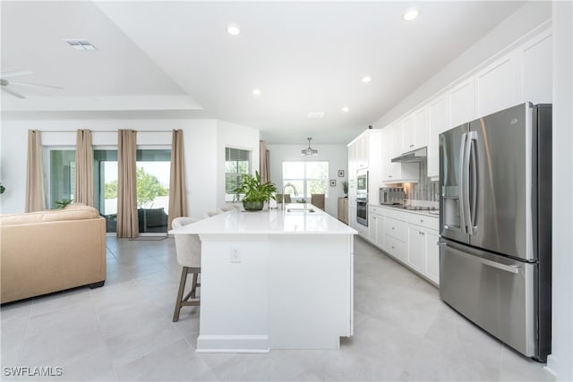 kitchen with a center island with sink, stainless steel appliances, white cabinets, sink, and a breakfast bar area