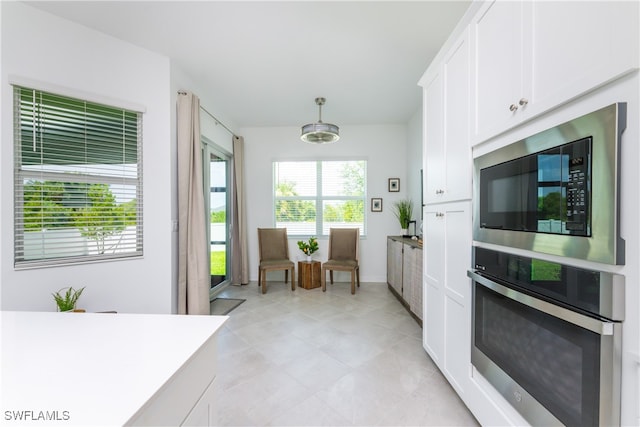 kitchen featuring stainless steel oven, white cabinetry, black microwave, and pendant lighting