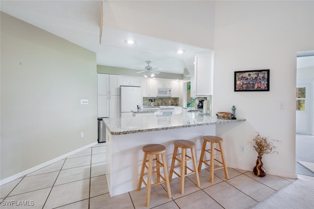 kitchen with a breakfast bar area, white cabinets, kitchen peninsula, and white appliances