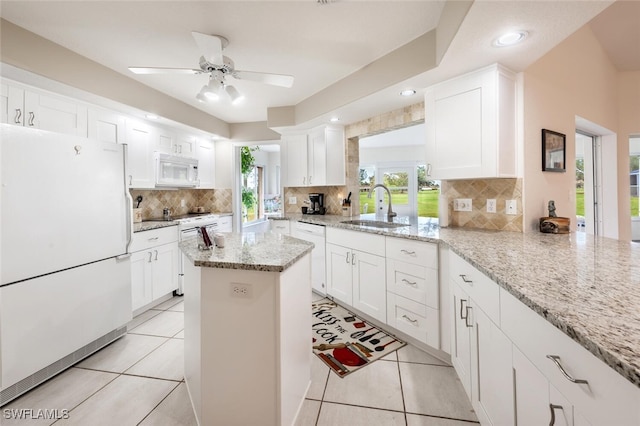 kitchen featuring tasteful backsplash, white cabinetry, light stone countertops, sink, and white appliances