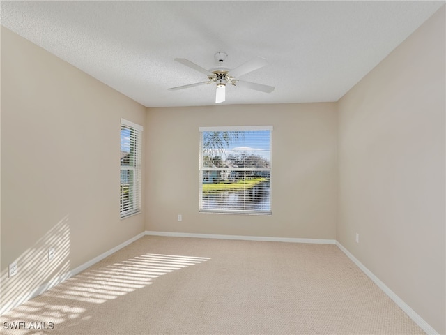 spare room with a textured ceiling, light colored carpet, a wealth of natural light, and ceiling fan