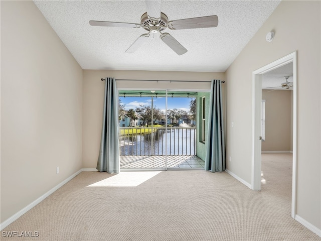 unfurnished room with ceiling fan, light colored carpet, a textured ceiling, and a water view