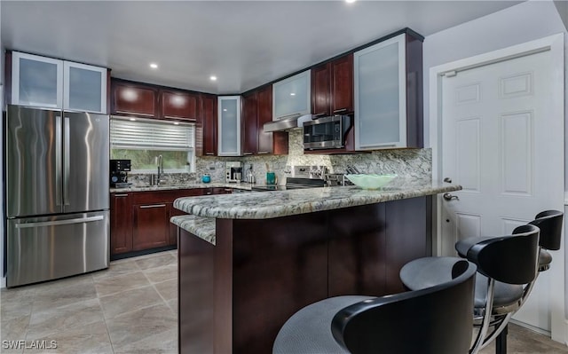 kitchen featuring sink, light stone countertops, appliances with stainless steel finishes, tasteful backsplash, and kitchen peninsula