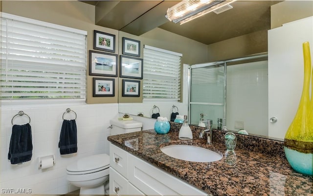 bathroom with walk in shower, vanity, toilet, and tile walls