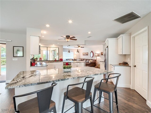 kitchen featuring a breakfast bar area, kitchen peninsula, light stone countertops, white cabinets, and dark hardwood / wood-style flooring