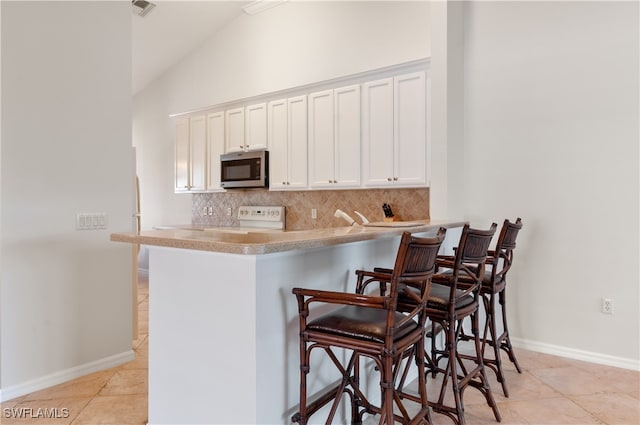 kitchen with lofted ceiling, decorative backsplash, a breakfast bar area, white cabinets, and white stove