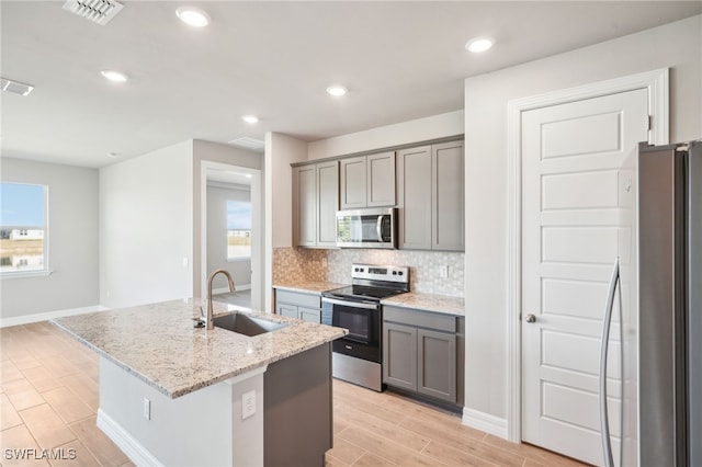 44290 Frontier Dr, Punta Gorda, FL 33982 - kitchen with appliances with stainless steel finishes, tasteful backsplash, sink, light stone counters, and a center island with sink
