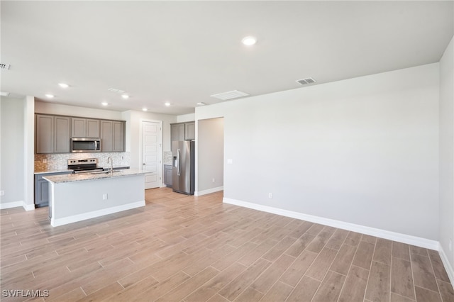 44290 Frontier Dr, Punta Gorda, FL 33982 - kitchen featuring gray cabinets, decorative backsplash, a kitchen island with sink, light stone counters, and stainless steel appliances