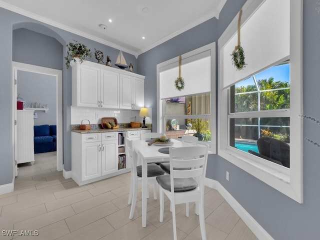 kitchen with white cabinetry, ornamental molding, backsplash, and light stone countertops