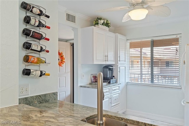 kitchen featuring white cabinets, ceiling fan, light stone counters, and ornamental molding