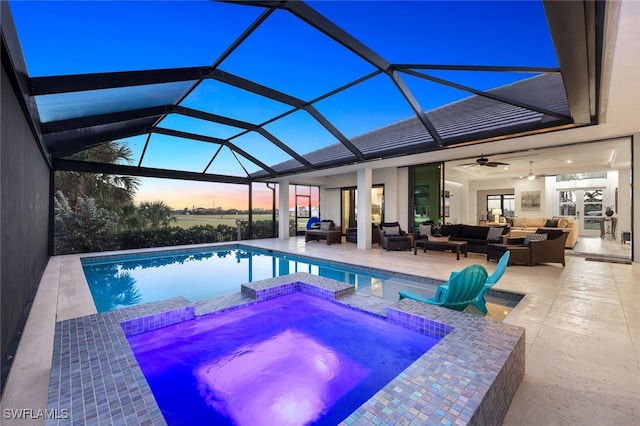 pool at dusk featuring an in ground hot tub, an outdoor hangout area, ceiling fan, glass enclosure, and a patio area