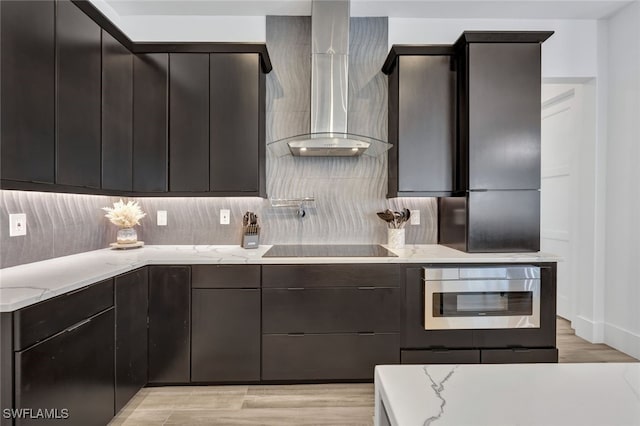 kitchen with light stone countertops, black electric stovetop, tasteful backsplash, wall chimney range hood, and light hardwood / wood-style flooring