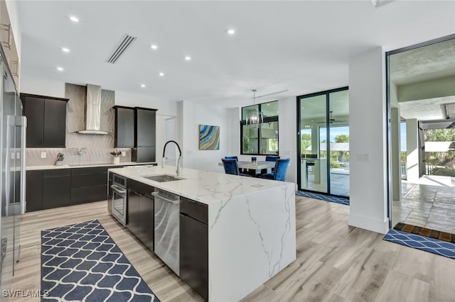 kitchen featuring light wood-type flooring, a center island with sink, wall chimney exhaust hood, and sink