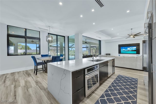 kitchen with oven, sink, decorative light fixtures, light stone countertops, and a large island