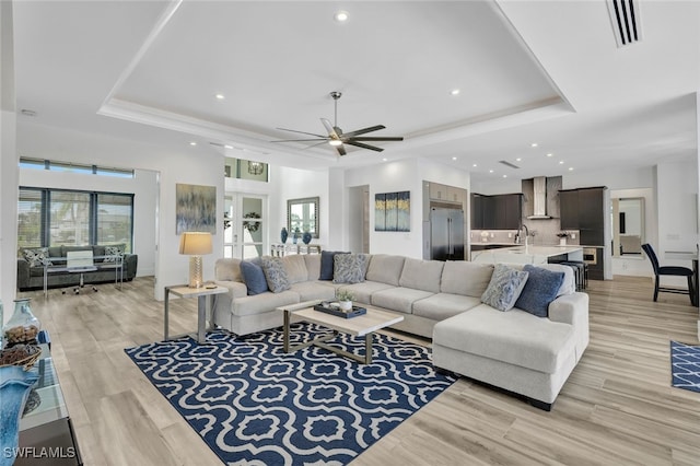 living room featuring ceiling fan, light wood-type flooring, french doors, and a tray ceiling