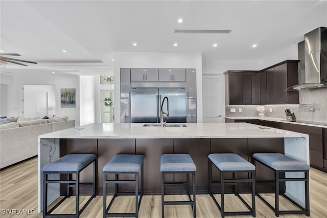 kitchen featuring a large island, stainless steel built in fridge, wall chimney exhaust hood, and light wood-type flooring