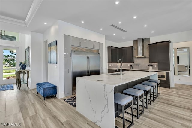 kitchen featuring a kitchen breakfast bar, stainless steel built in fridge, wall chimney range hood, sink, and a large island