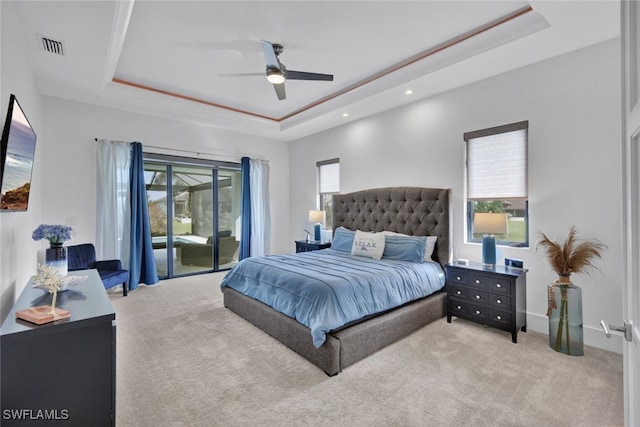 carpeted bedroom featuring ceiling fan, a raised ceiling, and multiple windows