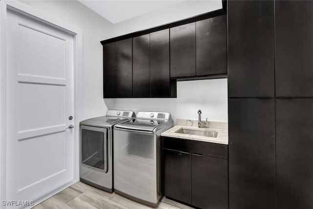 clothes washing area with cabinets, separate washer and dryer, light hardwood / wood-style floors, and sink