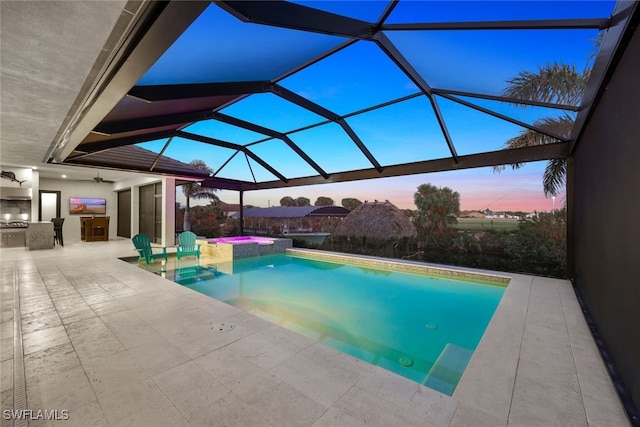 pool at dusk featuring area for grilling, a lanai, ceiling fan, a patio, and an outdoor bar