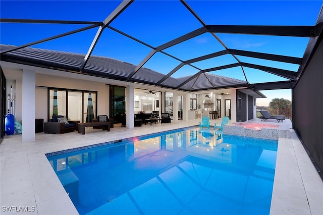 pool at dusk featuring glass enclosure, ceiling fan, an outdoor kitchen, an outdoor living space, and a patio