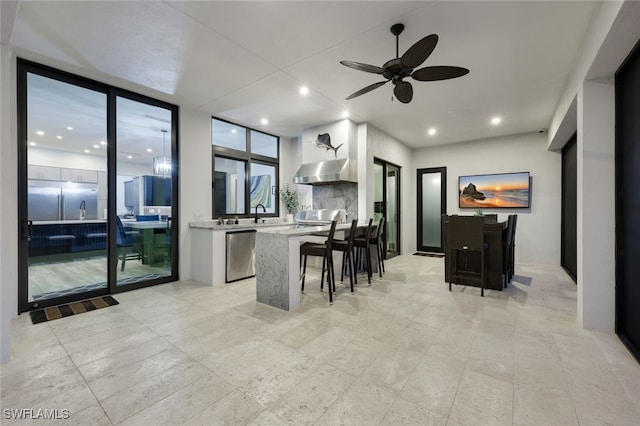 kitchen featuring white cabinets, a kitchen breakfast bar, expansive windows, stainless steel dishwasher, and range hood