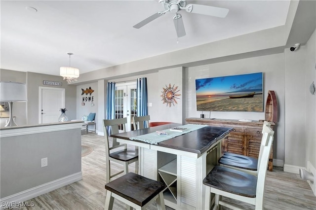 kitchen with decorative light fixtures, a kitchen breakfast bar, light wood-type flooring, and ceiling fan with notable chandelier