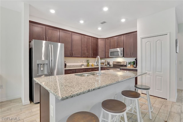 kitchen with light stone countertops, appliances with stainless steel finishes, sink, a kitchen breakfast bar, and a kitchen island with sink