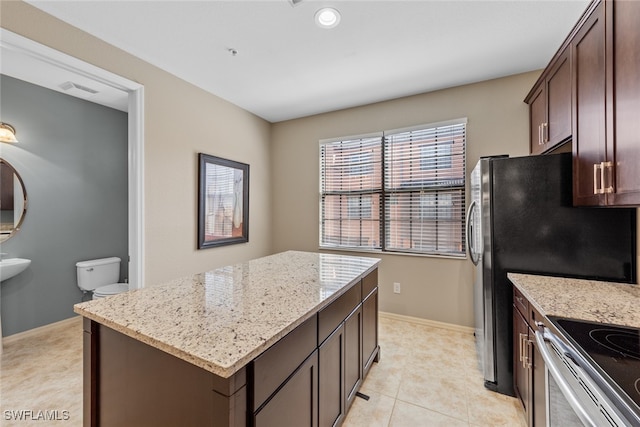 kitchen featuring a kitchen island, dark brown cabinets, stainless steel stove, light stone counters, and light tile patterned floors