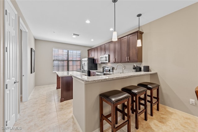 kitchen with kitchen peninsula, light stone counters, a kitchen breakfast bar, pendant lighting, and stainless steel appliances