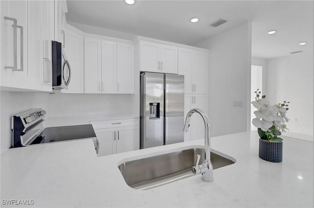 kitchen featuring white cabinets, appliances with stainless steel finishes, light stone counters, and sink