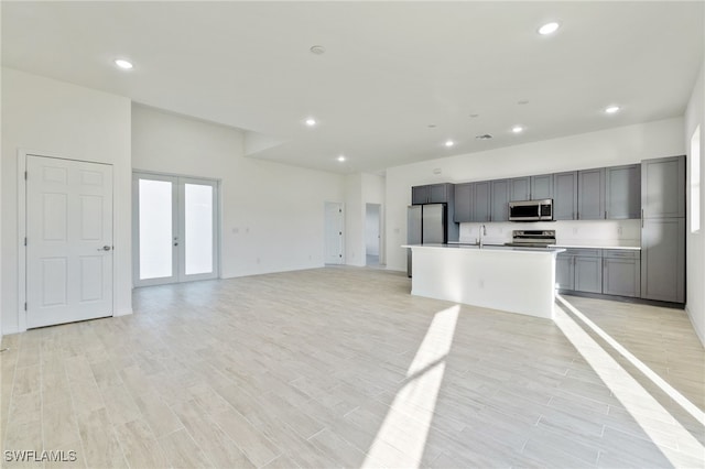 kitchen featuring a center island with sink, light wood-type flooring, gray cabinets, french doors, and stainless steel appliances