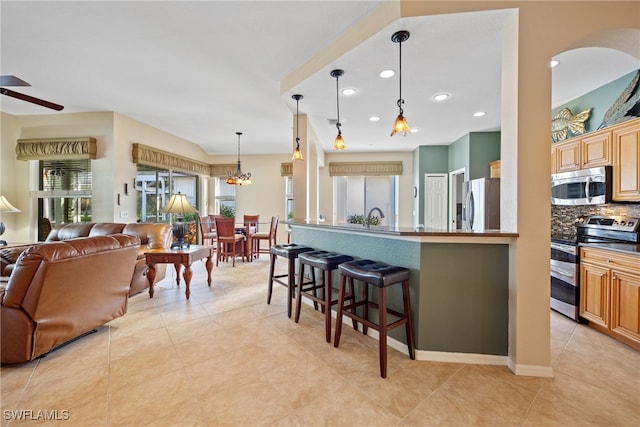 kitchen featuring decorative backsplash, light tile patterned flooring, a kitchen bar, pendant lighting, and appliances with stainless steel finishes