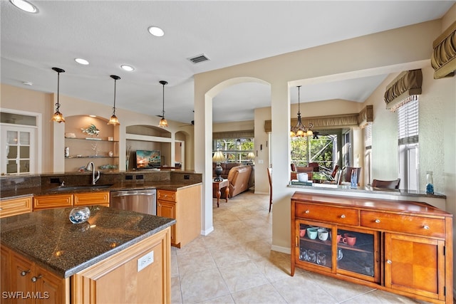 kitchen with sink, dark stone counters, pendant lighting, stainless steel dishwasher, and an inviting chandelier