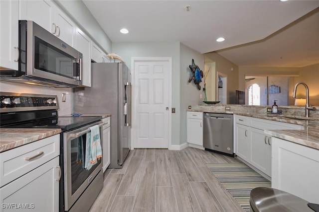 kitchen featuring light hardwood / wood-style flooring, sink, white cabinetry, appliances with stainless steel finishes, and light stone counters